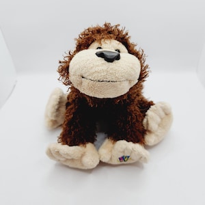 Könnte beinhalten: Ein braunes und beigefarbenes Plüsch-Affenspielzeug mit einer schwarzen Nase und einem fröhlichen Ausdruck. Das Spielzeug hat ein buntes "TY"-Etikett an seinem Fuß.