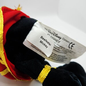 Op de afbeelding: Een Beefeater Mickey Mouse knuffel. Het speelgoed draagt een rood en goud uniform. Het label luidt "The Walt Disney Company" en "Beefeater Mickey".