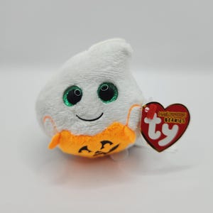 May include: White plush ghost with green eyes and a smiling face. The ghost is holding a small orange pumpkin with a jack-o'-lantern face. The ghost has a Ty tag attached to it that says "Halloween Beanies".