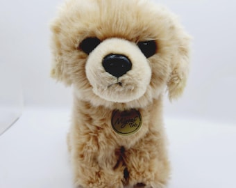 May include: A small, light brown plush dog toy with black eyes and a black nose. The toy has a gold tag with the text "Mymi Toys" on it.