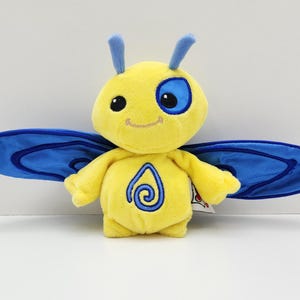 May include: A plush yellow butterfly toy with blue wings and antennae. The toy has a smiling face with a blue eye patch and a blue and white design on its chest. The wings are a vibrant blue color.
