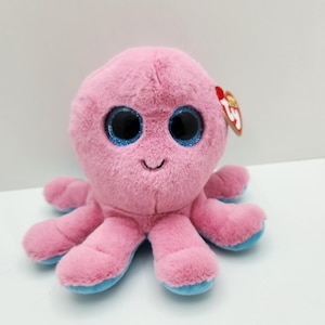 May include: A pink plush octopus toy with large, sparkly blue eyes and a smiling face. The tentacles are pink with blue tips. A red tag is attached to the toy.