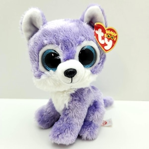 May include: A plush purple wolf toy with large blue eyes and a white muzzle. The stuffed animal has a red heart-shaped tag attached to its ear. The toy is sitting on a white surface.