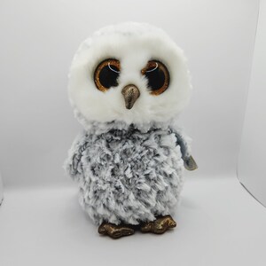 May include: A gray and white plush owl with large, glittery eyes. The owl has a small, orange beak and gold-colored feet.