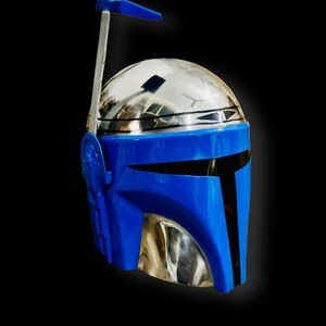 May include: A blue and silver Mandalorian helmet with a raised antenna. The helmet has a black visor and a blue faceplate.