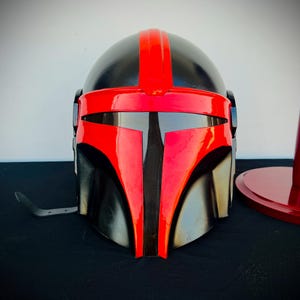 May include: A black and red helmet with a visor. The helmet has a red stripe down the center and a black visor.