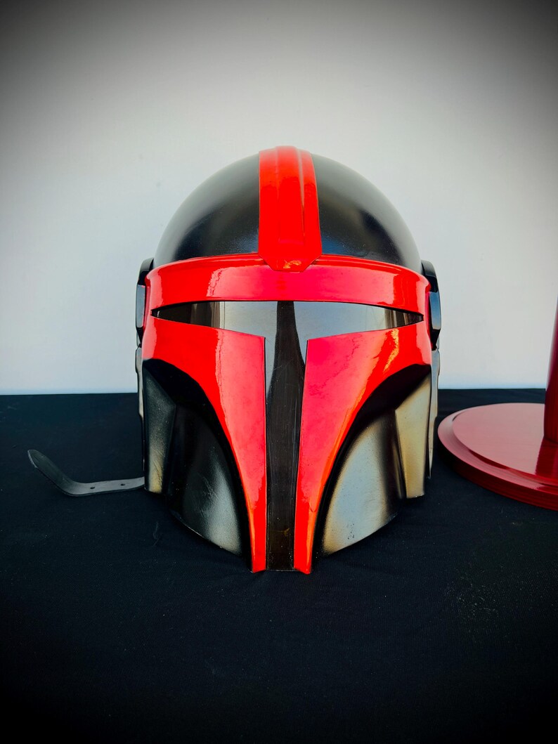 May include: A black and red helmet with a visor. The helmet has a red stripe down the center and a black visor.