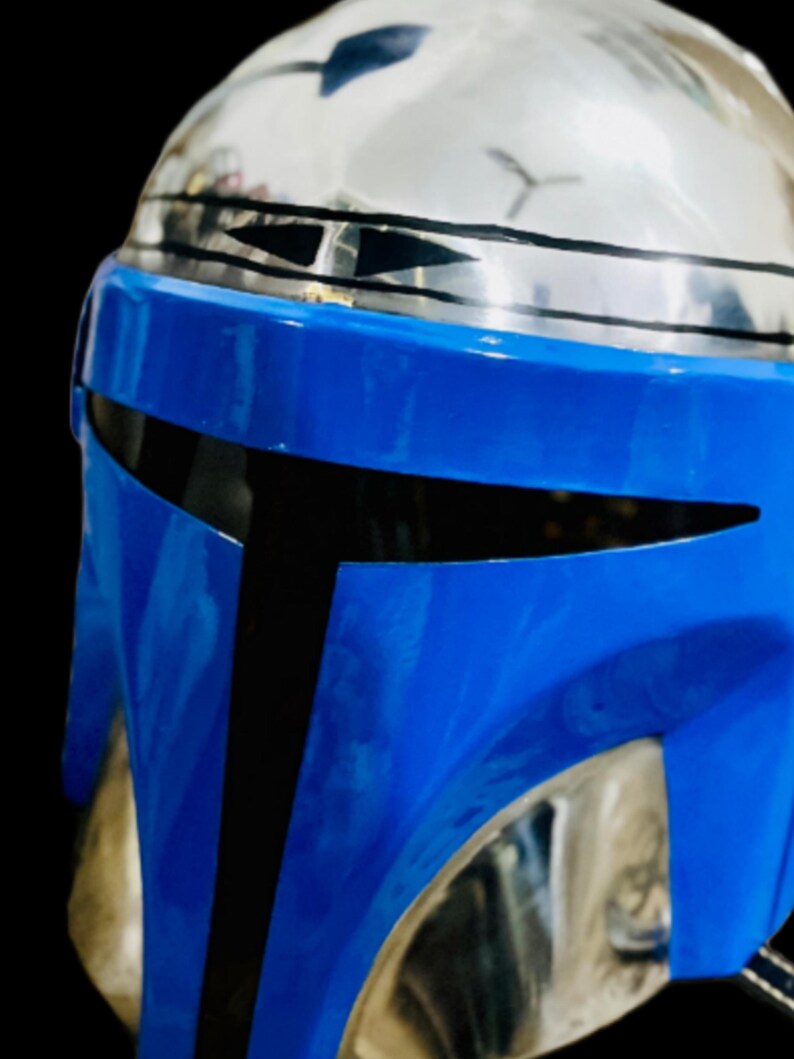 May include: A blue and black Mandalorian helmet with a silver visor. The helmet has a black stripe across the top and a black stripe across the bottom.