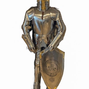 Puede incluir: Una armadura completa de plata y dorada con un escudo que presenta un caballero a caballo y el texto "OPSC" y "MILITIA" en un c&iacute;rculo. El escudo tambi&eacute;n tiene un dise&ntilde;o de nudo celta en la parte inferior.
