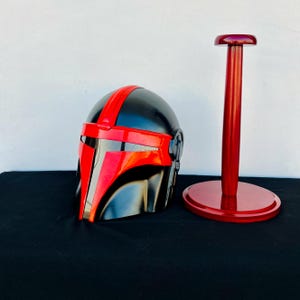May include: A black and red helmet with a red visor and a red stand. The helmet has a black and red design on the front.