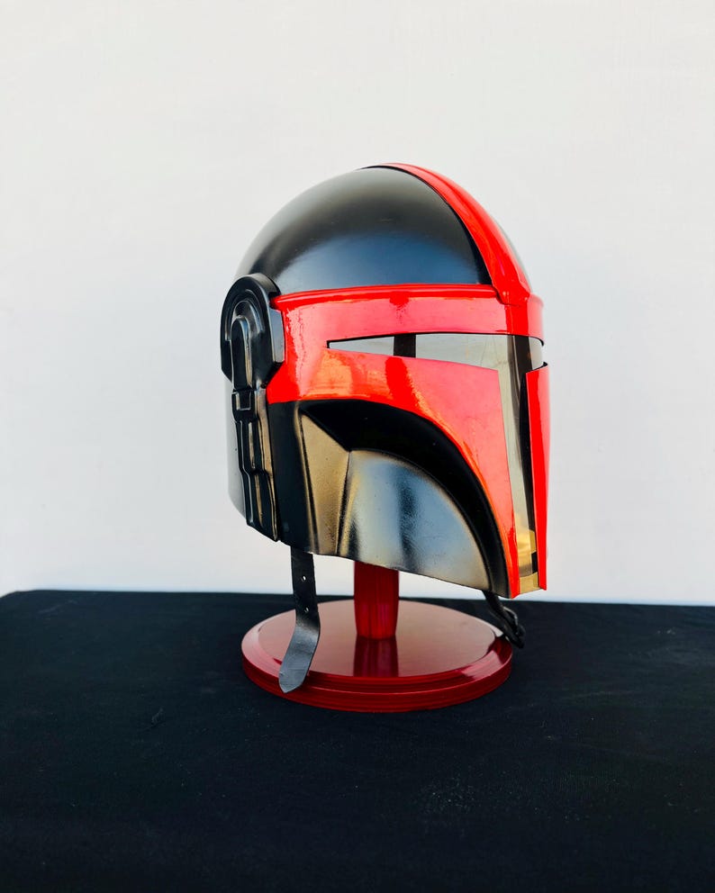 May include: A black and red helmet with a visor, displayed on a red stand. The helmet has a textured surface and a sleek design.