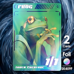 May include: A trading card featuring a stylized green frog with orange eyes, wearing a green and white outfit. The card reads "FROG" at the top and "TOKEN CREATURE" at the bottom. The card also displays "1/1", "2 Cards", and "Foil".