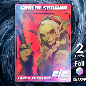 Op de afbeelding: Een holografische trading card met een groene goblin-sjaman met rode ogen en lang wit haar. De kaart heeft de titel "Goblin Shaman" en heeft een kracht en uithoudingsvermogen van 2/2. De kaart is gelabeld als "Token Creature" en heeft een folie afwerking.