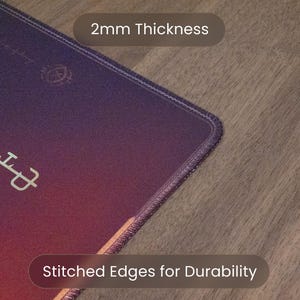 May include: A close-up of a purple and red mousepad with stitched edges for durability. The mousepad is 2mm thick. The mousepad has a design and text in a light green color.