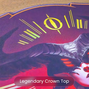 May include: A close-up of a purple and red graphic design with a face and horns. The design has yellow accents and the text "Legendary Crown Top" at the bottom. The image is on a wooden surface.