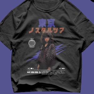 May include: A black crew neck t-shirt featuring a graphic print of a person with dark hair wearing a polka dot shirt. The design includes Japanese text, a wireframe globe, purple lightning bolts, and the text "TOKYO NOSTALGIA" and "SMART URBAN MINDS".