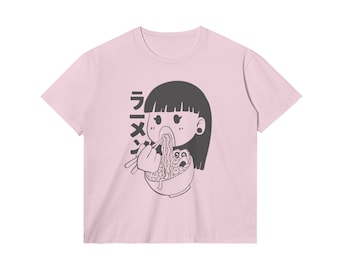 Könnte beinhalten: Ein hellrosa T-Shirt mit kurzen Ärmeln und einem schwarzen Grafikdruck einer Person mit dunklem Haar, die mit Stäbchen Nudeln aus einer Schüssel isst. Der japanische Text "ラーメン" ist links neben der Figur vertikal in Schwarz aufgedruckt.