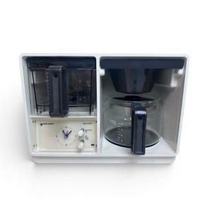 May include: A white Black & Decker Spacemaker coffee maker. The coffee maker has a clear glass carafe with a black handle, a black filter basket, and a water reservoir. It features a clock and control panel.
