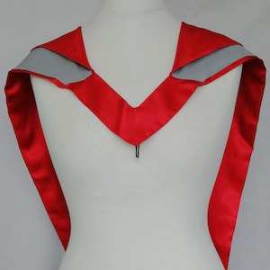 May include: Red graduation stole with a grey velvet trim. The stole is made of satin and has a V-shaped neckline.