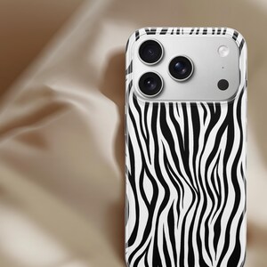 May include: A smartphone case with a zebra print design. The case features a black and white pattern of vertical stripes, with a clear border. The phone's camera lenses are visible at the top.
