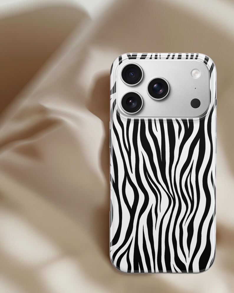 May include: A smartphone case with a zebra print design. The case features a black and white pattern of vertical stripes, with a clear border. The phone's camera lenses are visible at the top.
