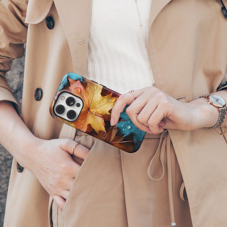 May include: A smartphone case featuring a colorful autumn leaf design with water droplets. The case has a black border and a glossy finish. The leaves are in shades of yellow, orange, and blue.