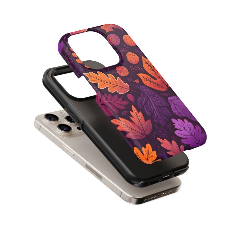 May include: A smartphone with a black case and a decorative cover featuring a fall leaves pattern in shades of purple, orange, and red. The phone case is designed to protect the device while adding a stylish touch.