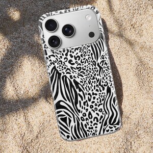 May include: A smartphone case with a black and white animal print design. The case features a combination of zebra stripes and leopard spots. The phone case is on a sandy surface.
