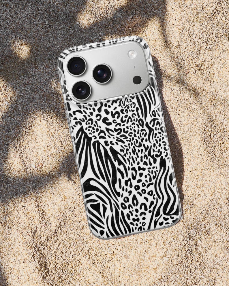 May include: A smartphone case with a black and white animal print design. The case features a combination of zebra stripes and leopard spots. The phone case is on a sandy surface.