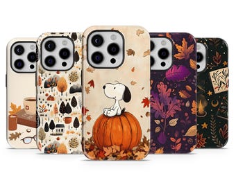 May include: A collection of five phone cases with autumn-themed designs. One case features Snoopy sitting on a pumpkin. Other cases display fall leaves, trees, and a cup of coffee. The cases have a glossy finish.