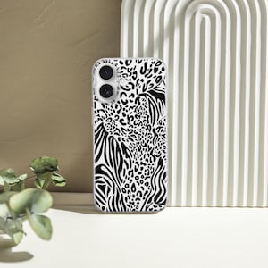 May include: A clear phone case featuring a black and white animal print design. The pattern combines zebra stripes, leopard spots, and other abstract shapes. The case is shown standing upright against a white, arched background.
