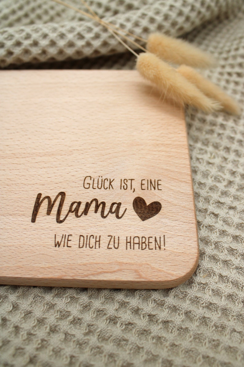 Może przedstawiać: Drewniana deska do krojenia z wygrawerowanym tekstem "Gl&uuml;ck ist, eine Mama wie dich zu haben!" Tekst jest w języku niemieckim i oznacza "Szczęście to mieć mamę taką jak ty!"