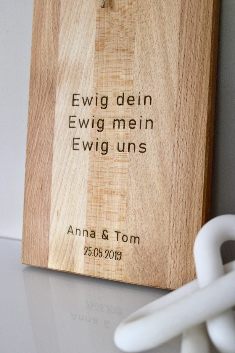 May include: A wooden cutting board with the text "Ewig dein Ewig mein Ewig uns" and "Anna & Tom 25.05.2019" engraved on it.