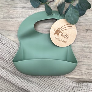 May include: A green silicone baby bib with a wooden tag that says "hello little one" with a starfish and shooting star design.