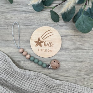 May include: A wooden baby announcement disc with a star and shooting star design. The disc says "hello little one". A wooden and silicone teething toy with a green silicone bead chain is also pictured.