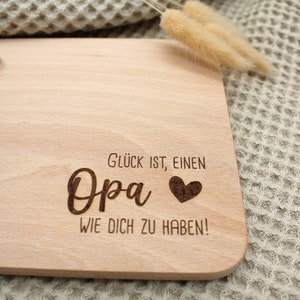 Może przedstawiać: Drewniana deska do krojenia z tekstem "Gl&uuml;ck ist, einen Opa wie dich zu haben!" i wygrawerowanym sercem.