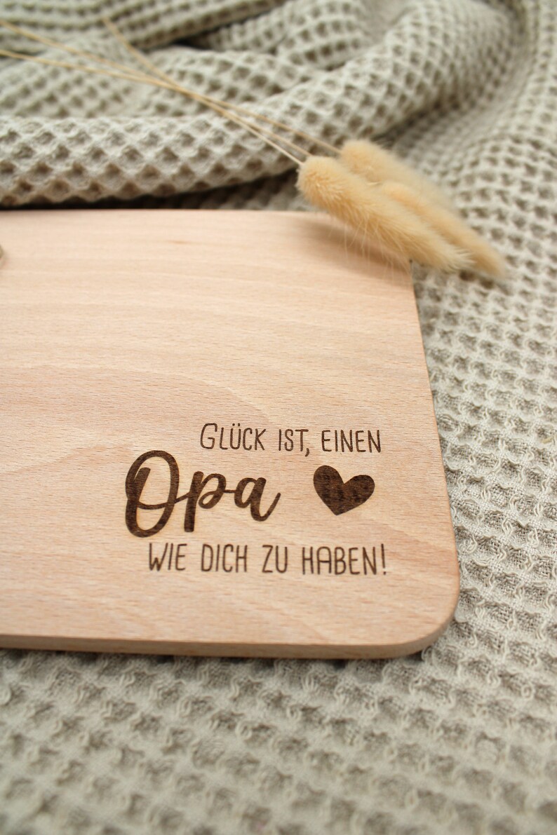Może przedstawiać: Drewniana deska do krojenia z tekstem "Gl&uuml;ck ist, einen Opa wie dich zu haben!" i wygrawerowanym sercem.