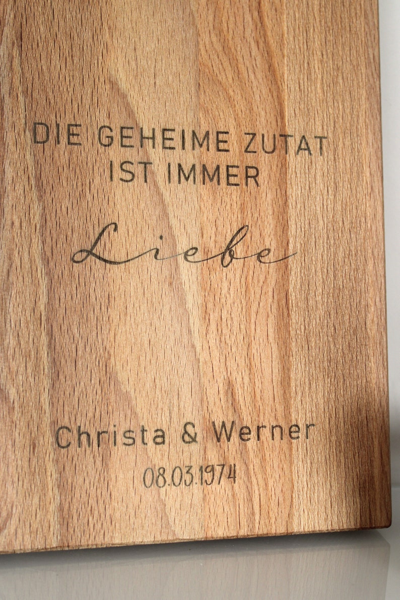 May include: A wooden cutting board with the text "DIE GEHEIME ZUTAT IST IMMER Liebe" and "Christa & Werner 08.03.1974" engraved on it.