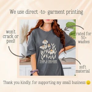 May include: A dark gray t-shirt with a floral design and the text "Take a chance cause you might grow".