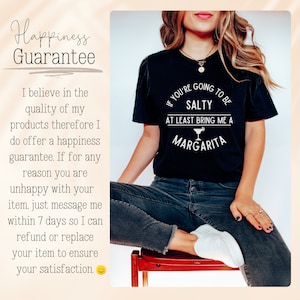May include: Black t-shirt with white text that reads "If you're going to be salty at least bring me a margarita". The text is in a circle with a margarita glass icon. A woman is wearing the shirt and sitting on a wooden chair.