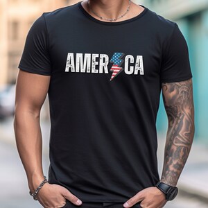 May include: A black t-shirt with a white graphic of the word "AMERICA" with an American flag lightning bolt design.
