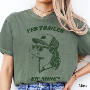 May include: Moss green t-shirt with the text "YER TRAILER ER' MINE?" above and below a graphic of a rodent wearing sunglasses and a trucker hat. The rodent has a cigarette in its mouth. The shirt is a casual style.