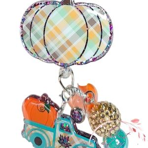 Op de afbeelding: Een herfst-thema badge reel met een pompoenvormige bovenkant met een ruitpatroon en glitterrand. Een turquoise vrachtwagen vervoert een oranje pompoen. Extra bedels zijn onder meer oranje en gouden kralen.