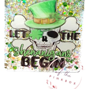 May include: A glittery green, white, and black square coaster with a skull wearing a green leprechaun hat and a shamrock over one eye. The text "Let the Shenanigans Begin" is written on the coaster.