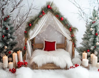 May include: A white faux fur bed with a red pillow inside a wooden canopy decorated with a garland of pine branches and red ornaments. The canopy is set against a snowy backdrop with two frosted Christmas trees and lit candles.