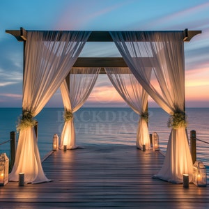 May include: A wooden wedding archway draped with white sheer fabric, decorated with greenery and lanterns, stands on a wooden dock overlooking a calm ocean at sunset.
