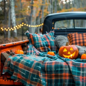 Può includere: Il cassone di un pick-up vintage decorato per Halloween con una coperta a quadri, cuscini e una zucca intagliata. Il pick-up è parcheggiato in una zona boscosa con foglie autunnali e luci a catena.