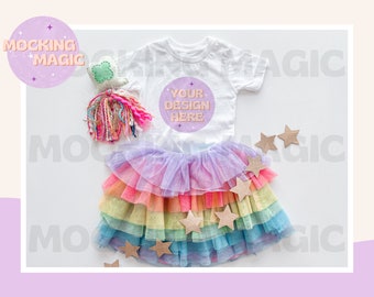 Op de afbeelding: Een wit baby onesie met de tekst "Your design here" op de voorkant, gecombineerd met een regenboog tutu rok en gouden ster decoraties.