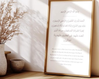 May include: A framed print with Arabic calligraphy and English translation. The print has a light-colored wooden frame and is displayed on a wooden surface. A vase with dried plants and a small bowl are in the foreground.