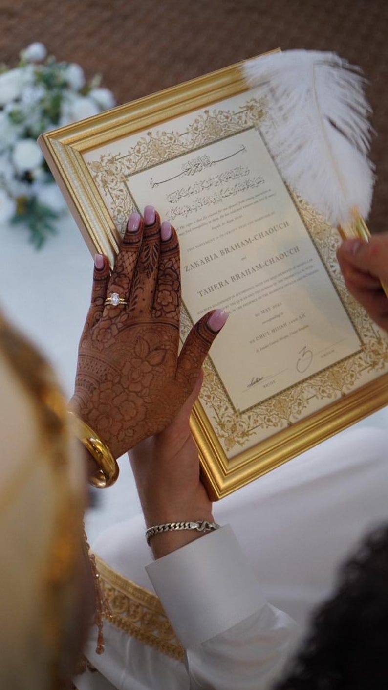 Może przedstawiać: Złota rama z aktem małżeństwa ozdobiona misternymi dekoracyjnymi obramowaniami i arabską kaligrafią u g&oacute;ry. Dokument zawiera nazwiska Zakaria Braham-Chaouch i Tahera Braham-Chaouch, datowany na 30 maja 2017 roku, wraz z białym pi&oacute;rem do pisania.